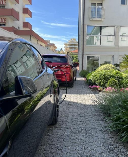 Auto elettrica in ricarica, giardino fiorito, atmosfera serena e luminosa.